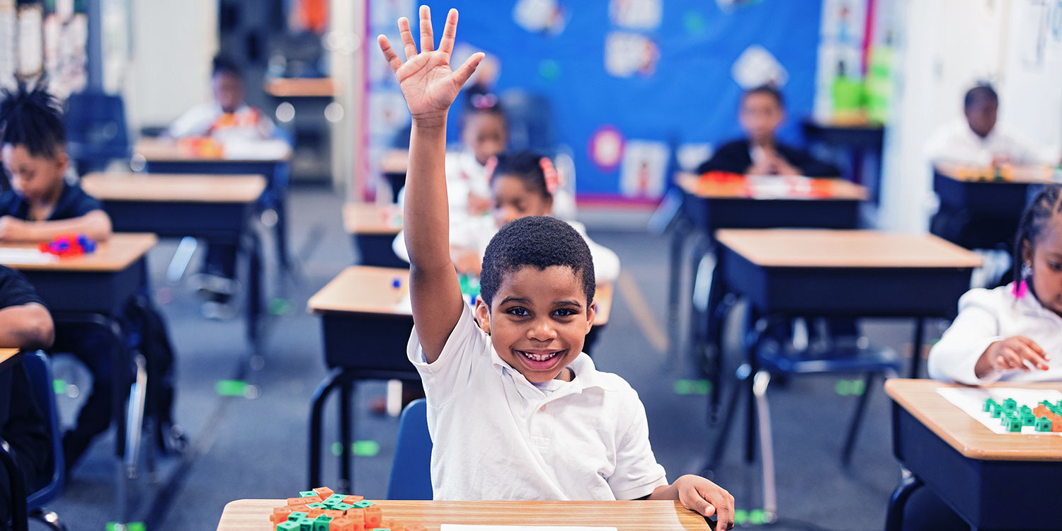 Smiling student with raised hand in a classroom.
